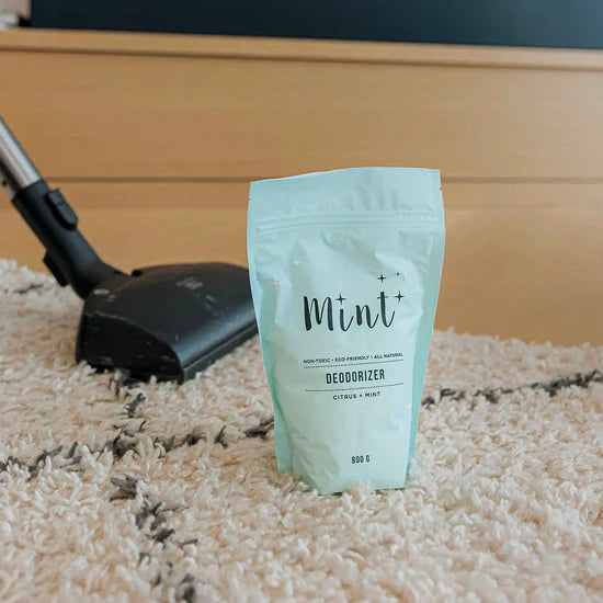 Mint Cleaning Carpet Deodorizer in it’s signature mint coloured packaging on a newly cleaned carpet with a vacuum in the back