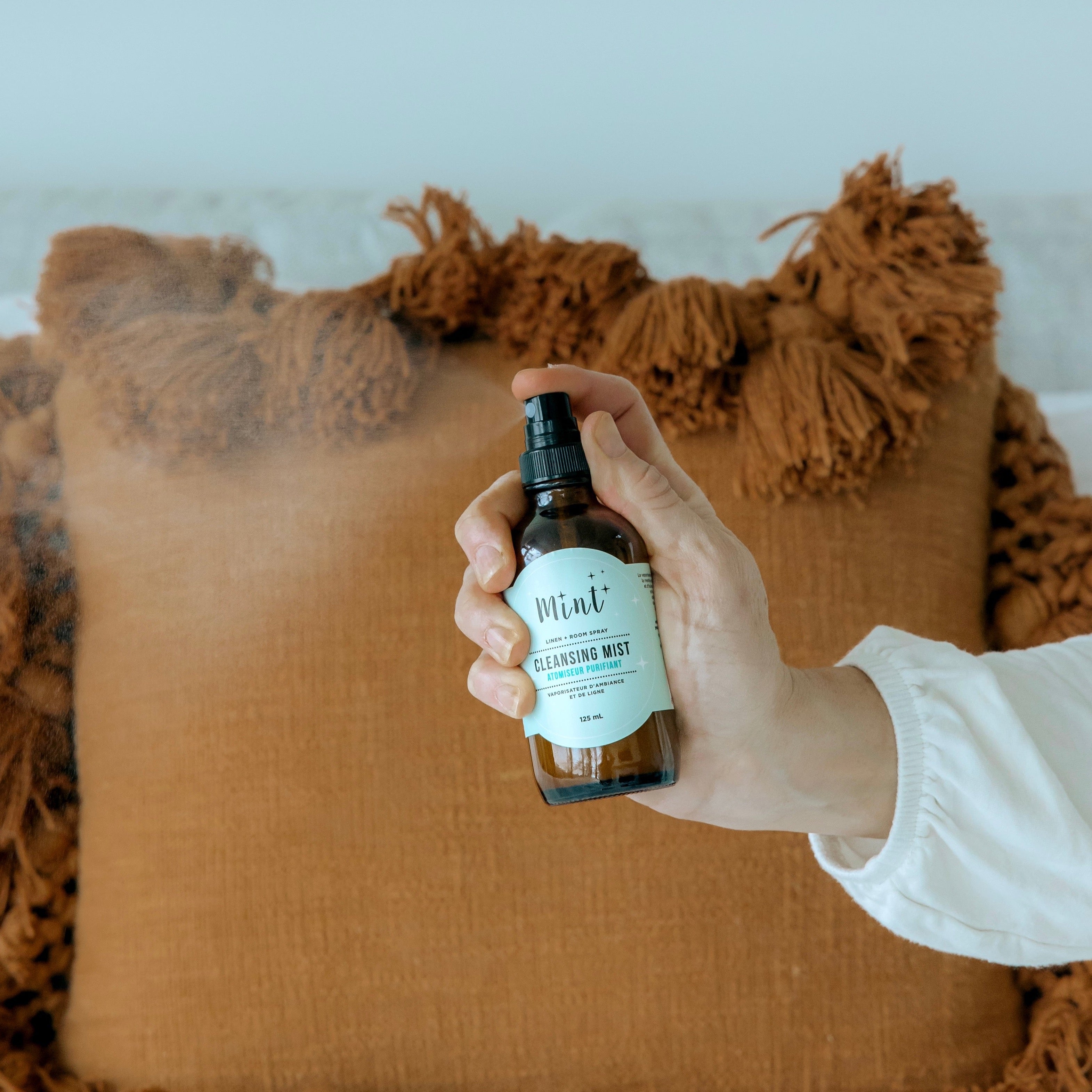 Hand sprays the mint cleaning cleansing mist room spray into a room and onto a pillow