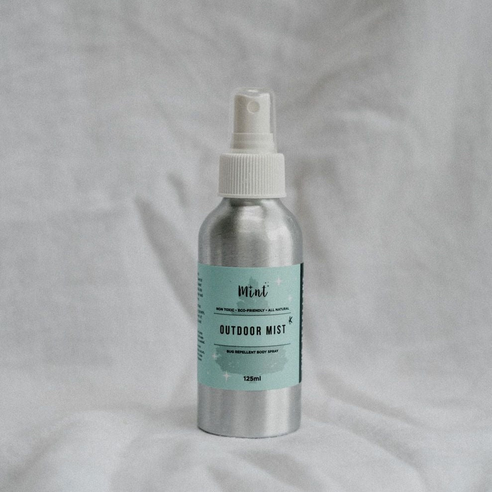 Mint Cleaning’s Outdoor Mist [bug spray] in an aluminum spray bottle with a cloth backdrop 
