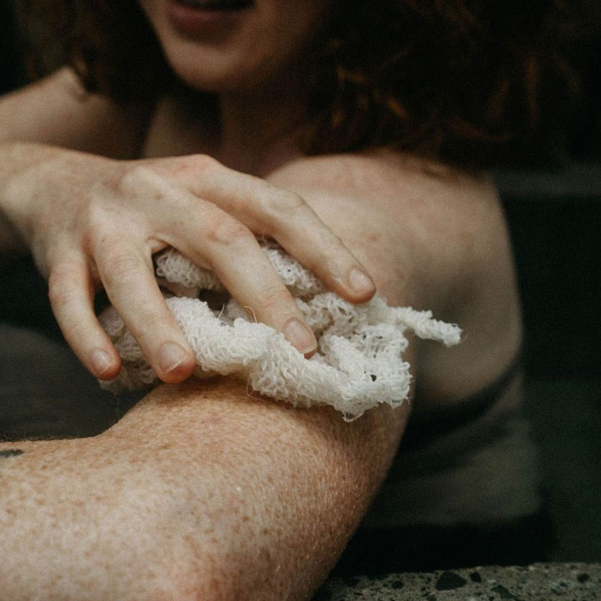 A woman is using a wet agave body cloth to wash her arms in the shower