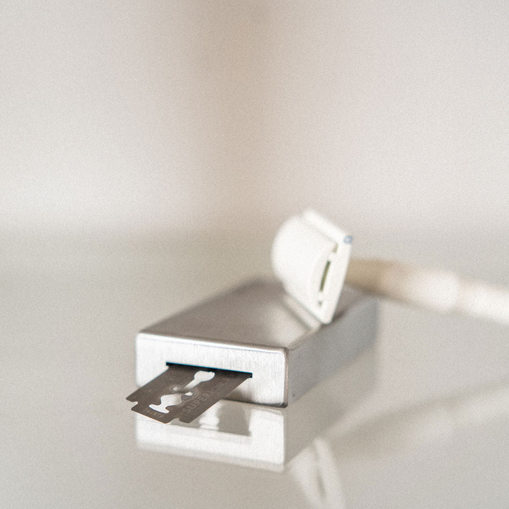 A razor blade is half inserted into the Well Kept blade bank to helpfully display how to safely dispose of old blades. A well kept safety razor sits on top of the bank