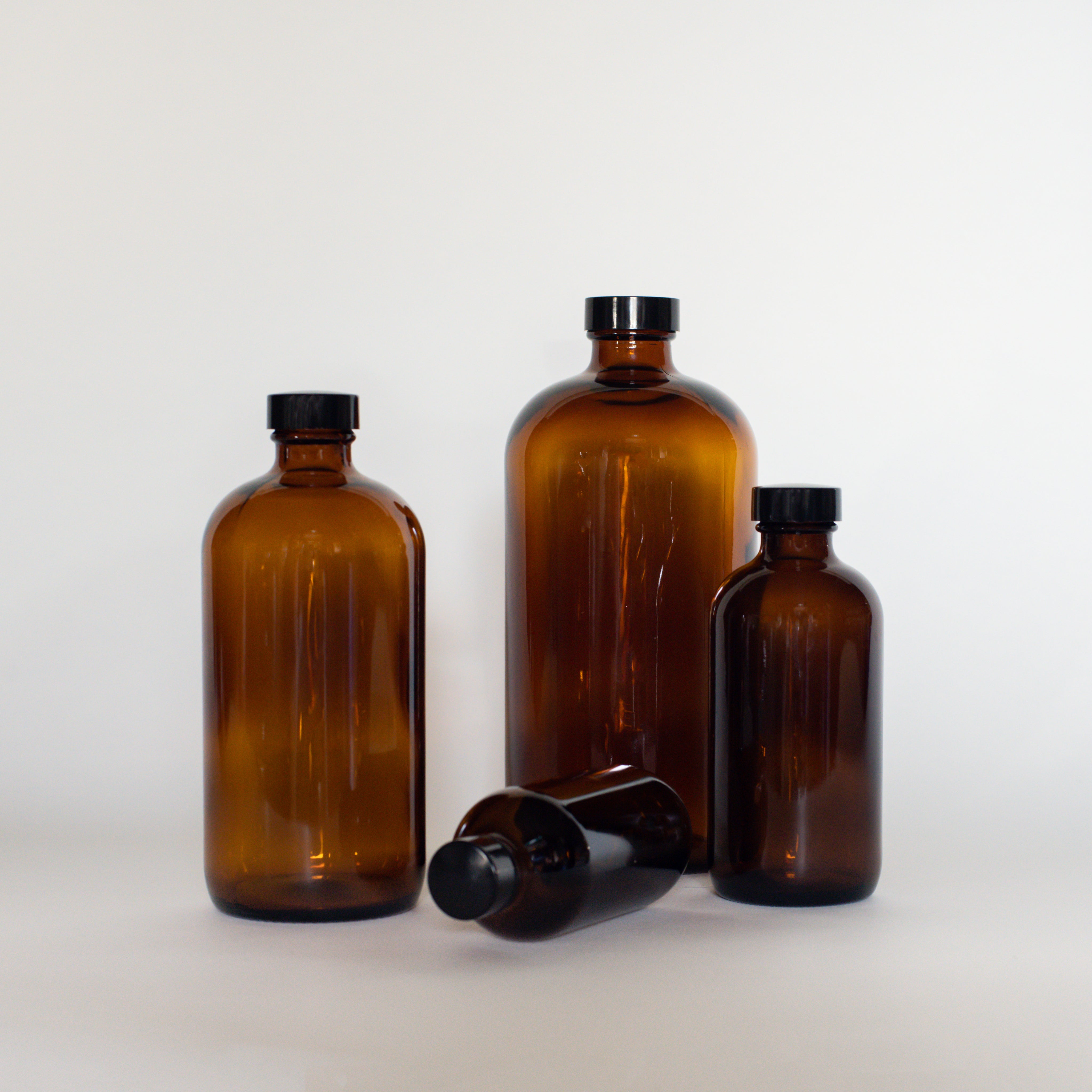 A variety of the Den refillery amber glass bottles are posed on a white surface with a white background.