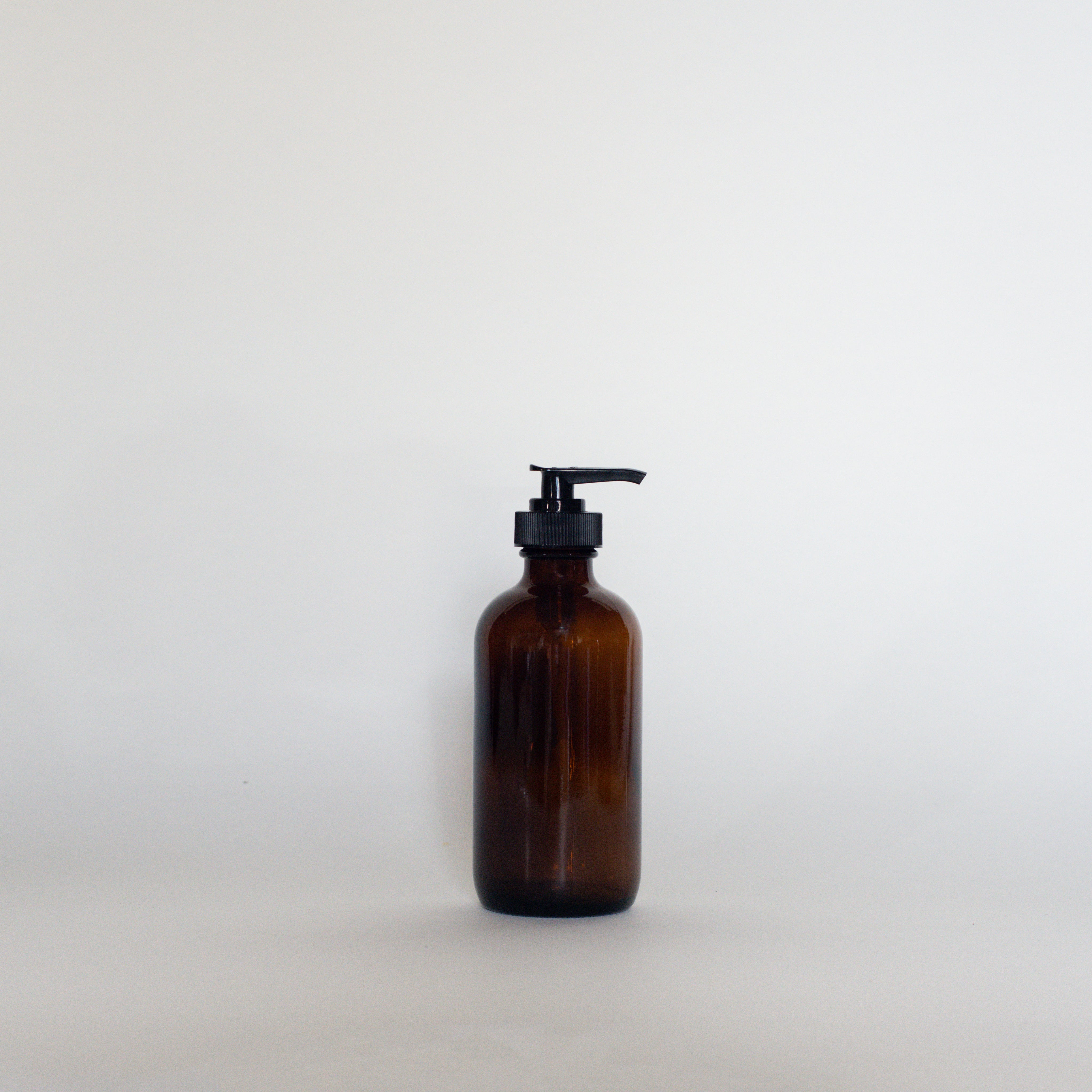 A 250ml amber glass bottle with a pump top sits on a white surface with a white background