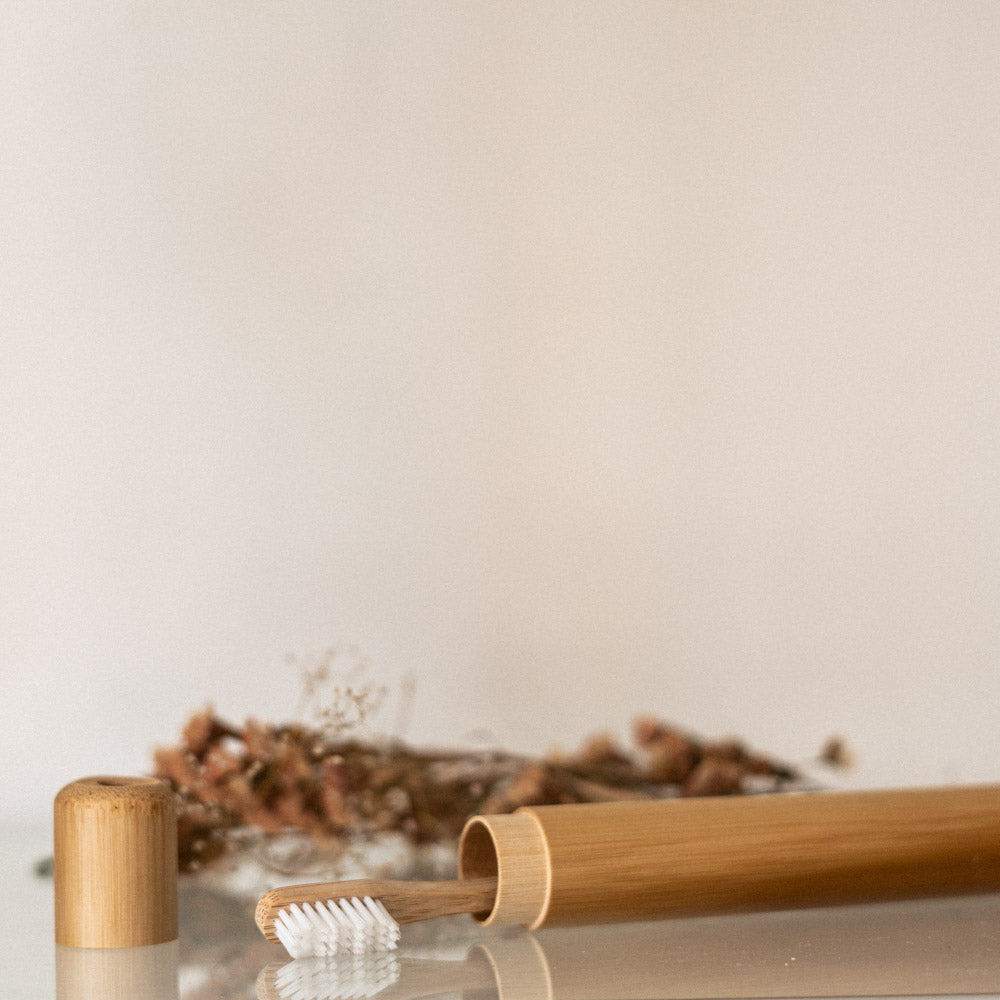 The all-natural bamboo toothbrush travel case is opened on a glass surface with a bamboo toothbrush inside